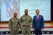 260504-N-KC192-1026 PORTSMOUTH, Va. (May 4, 2026) Lt. Raymond Jordan, center., assigned to Naval Medical Forces Atlantic, is presented the Junior Logistician of the Year Award by Dr. Michael McGinnis, Bureau of Medicine and Surgery (BUMED) executive director, during the 2026 Medical Logistics Symposium held on board Naval Medical Center Portsmouth, May 4, 2026. Jordan was recognized for improving logistics processes and managing deployment-ready medical materiel, strengthening the speed, accountability and effectiveness of expeditionary medical support. The Navy Medicine Logistics Symposium aims to maintain a common operating picture and update the Medical Logistics community reagarding the fiscal year 2026 Navy Medicine Campaign Order and the Navy MEDLOG goal to build a logistics system that delivers ready operational units to support the Naval Strategy. (U.S. Navy photo by Mass Communication Specialist Second Class Levi Decker)