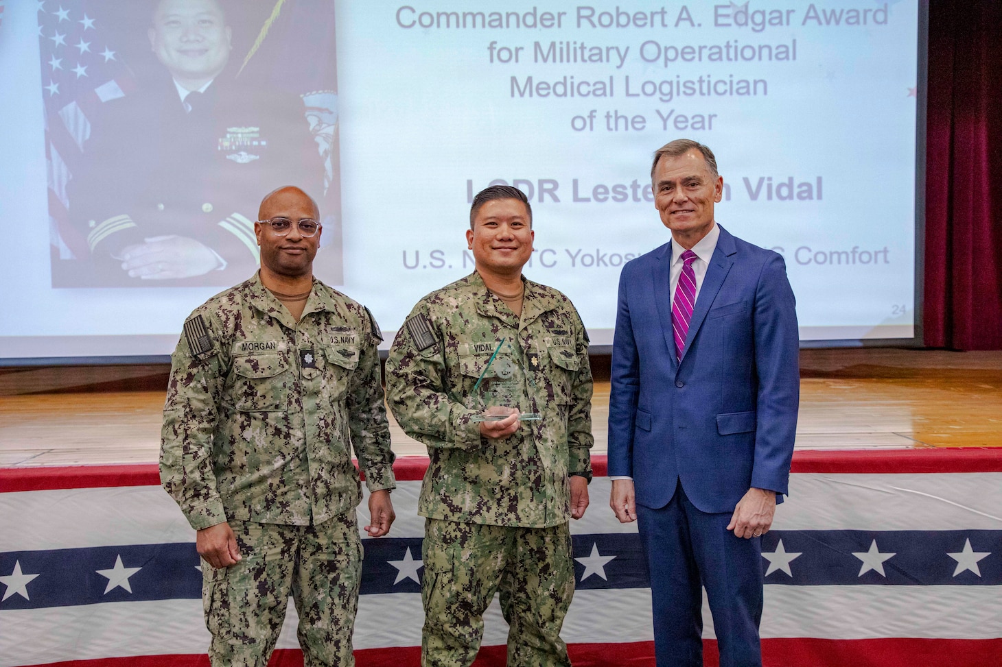260504-N-KC192-1026 PORTSMOUTH, Va. (May 4, 2026) Cmdr. Lester Vidal, center, assigned to the Mercy-class hospital ship USNS Comfort (T-AH 20), is presented the Commander Robert A. Edgar Award for Military Operational Medical Logistician of the Year by Dr. Michael McGinnis, Bureau of Medicine and Surgery (BUMED) executive director, during the 2026 Medical Logistics Symposium held on board Naval Medical Center Portsmouth, May 4, 2026. Vidal was recognized for leading large-scale medical logistics operations and delivering critical supplies during global missions, directly enabling sustained patient care and operational reach in expeditionary environments. The Navy Medicine Logistics Symposium aims to maintain a common operating picture and update the Medical Logistics community regarding the fiscal year 2026 Navy Medicine Campaign Order and the Navy MEDLOG goal to build a logistics system that delivers ready operational units to support the Naval Strategy. (U.S. Navy photo by Mass Communication Specialist Second Class Levi Decker)