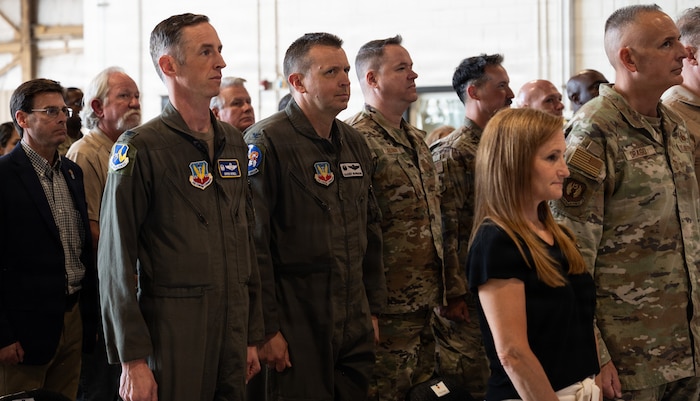 Airmen and civilians stand in rows of seats