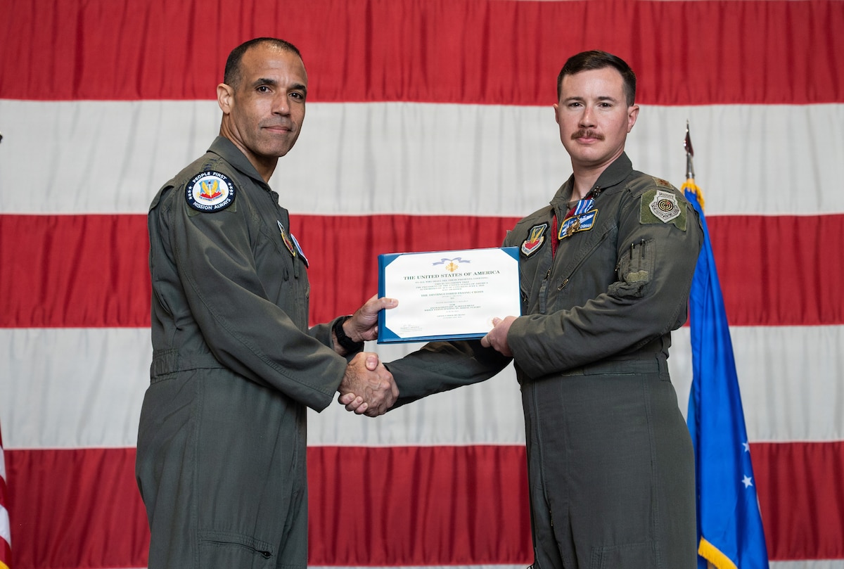 Two Air Force pilots hold a certificate with a giant American flag in the background