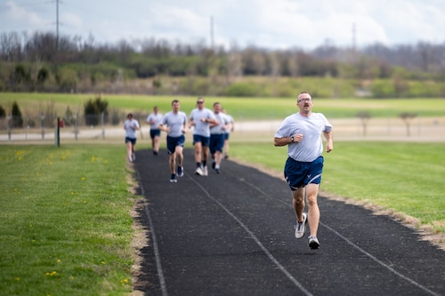 A small group, wearing Air Force fitness attire, run on a black track