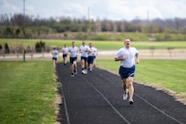 A small group, wearing Air Force fitness attire, run on a black track