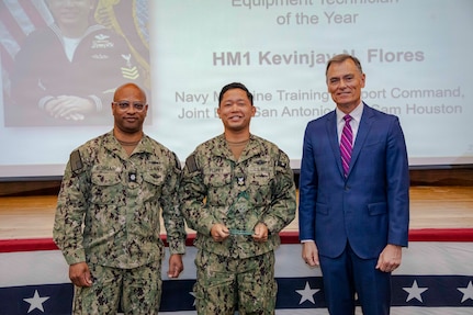 260504-N-KC192-1041 PORTSMOUTH, Va. (May 4, 2026) Hospital Corpsman 1st Class Kevinjay Flores, center, assigned to the Medical Education and Training Campus, is presented the Shore-Based Biomedical Equipment Technician of the Year Award by Dr. Michael McGinnis, Bureau of Medicine and Surgery (BUMED) executive director, during the 2026 Medical Logistics Symposium held on board Naval Medical Center Portsmouth, May 4, 2026. Flores was recognized for training the next generation of technicians, strengthening the technical readiness and reliability of equipment supporting deployed medical forces. The Navy Medicine Logistics Symposium aims to maintain a common operating picture and update the Medical Logistics community regarding the fiscal year 2026 Navy Medicine Campaign Order and the Navy MEDLOG goal to build a logistics system that delivers ready operational units to support the Naval Strategy. (U.S. Navy photo by Mass Communication Specialist Second Class Levi Decker)