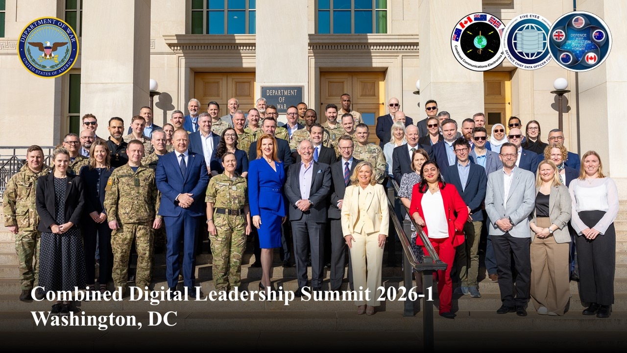 A large group poses for a photo on the steps of the Pentagon during the day.