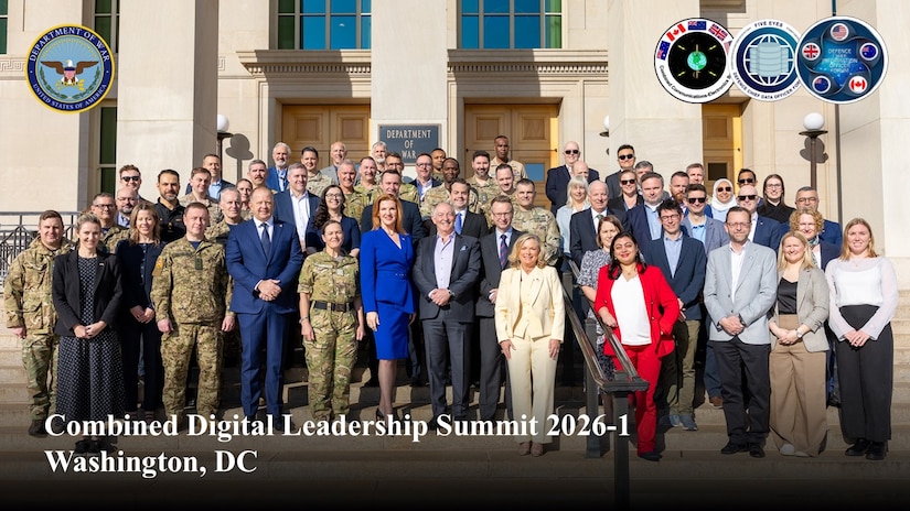 A large group poses for a photo on the steps of the Pentagon during the day.
