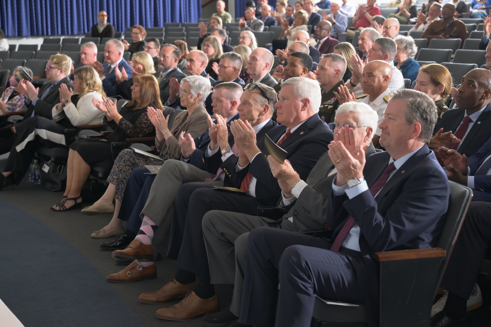 Several seated rows of audience members facing an off-camera stage in an auditorium.