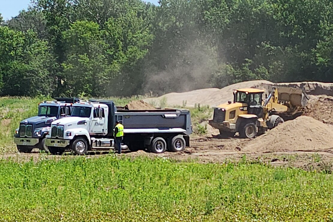 Dump trucks line up to be loaded with sand from a dredge material placement site.
