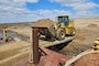A loader carries sand from a barge into a dredge material placement site along the river.
