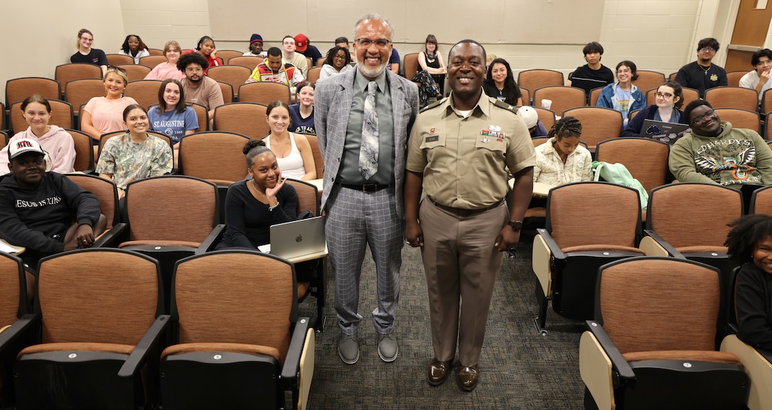 Picture of two men standing in an auditorium of students.
