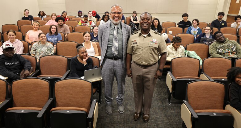 Picture of two men standing in an auditorium of students.