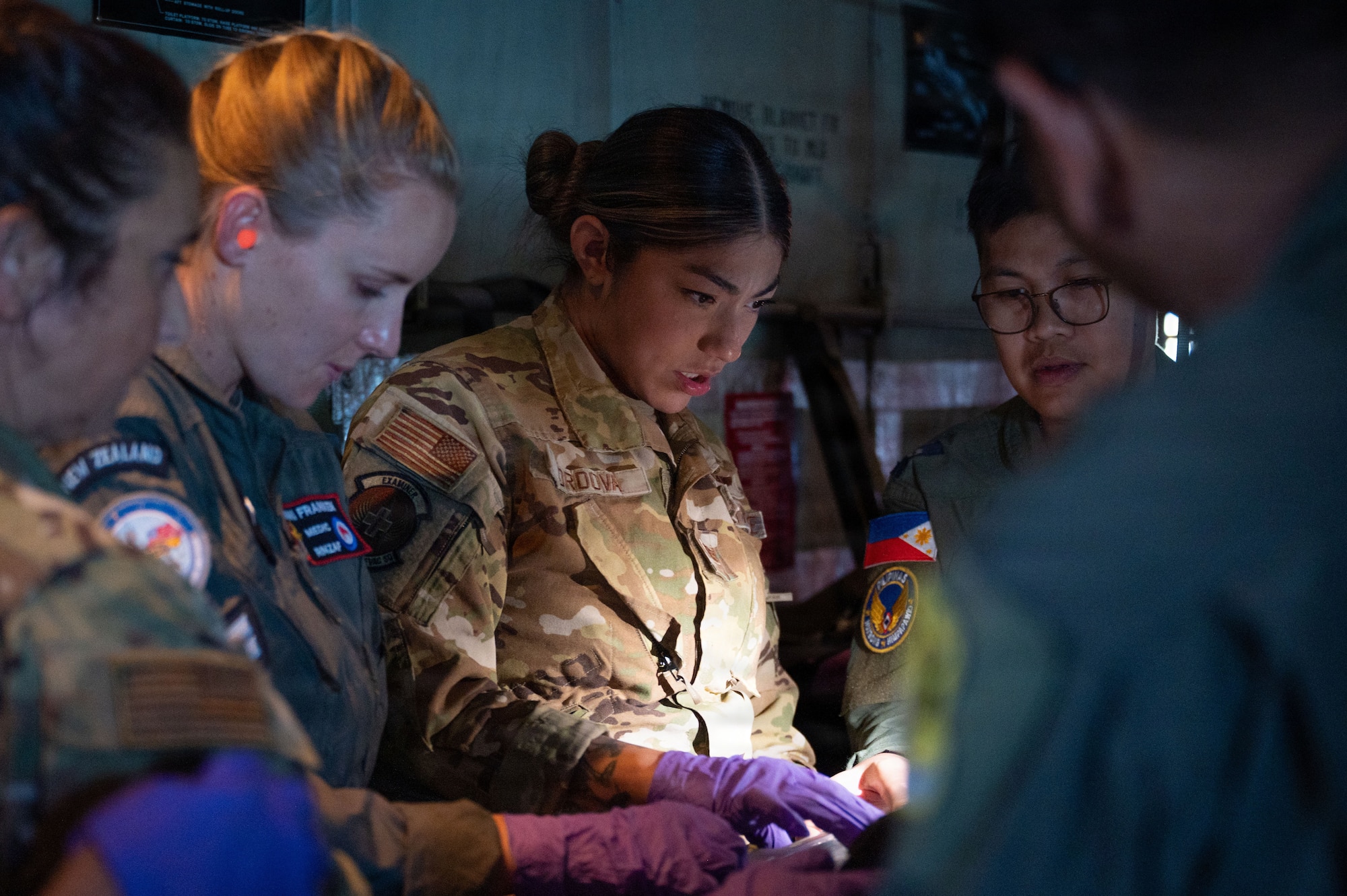 Royal New Zealand Air Force Cpl. Danielle Franken, U.S. Air Force Staff Sgt. Elena Cordova, and Philippine Air Force Maj. Jonald Suede work closely together, illuminated by a light as they organize medical supplies inside an aircraft.