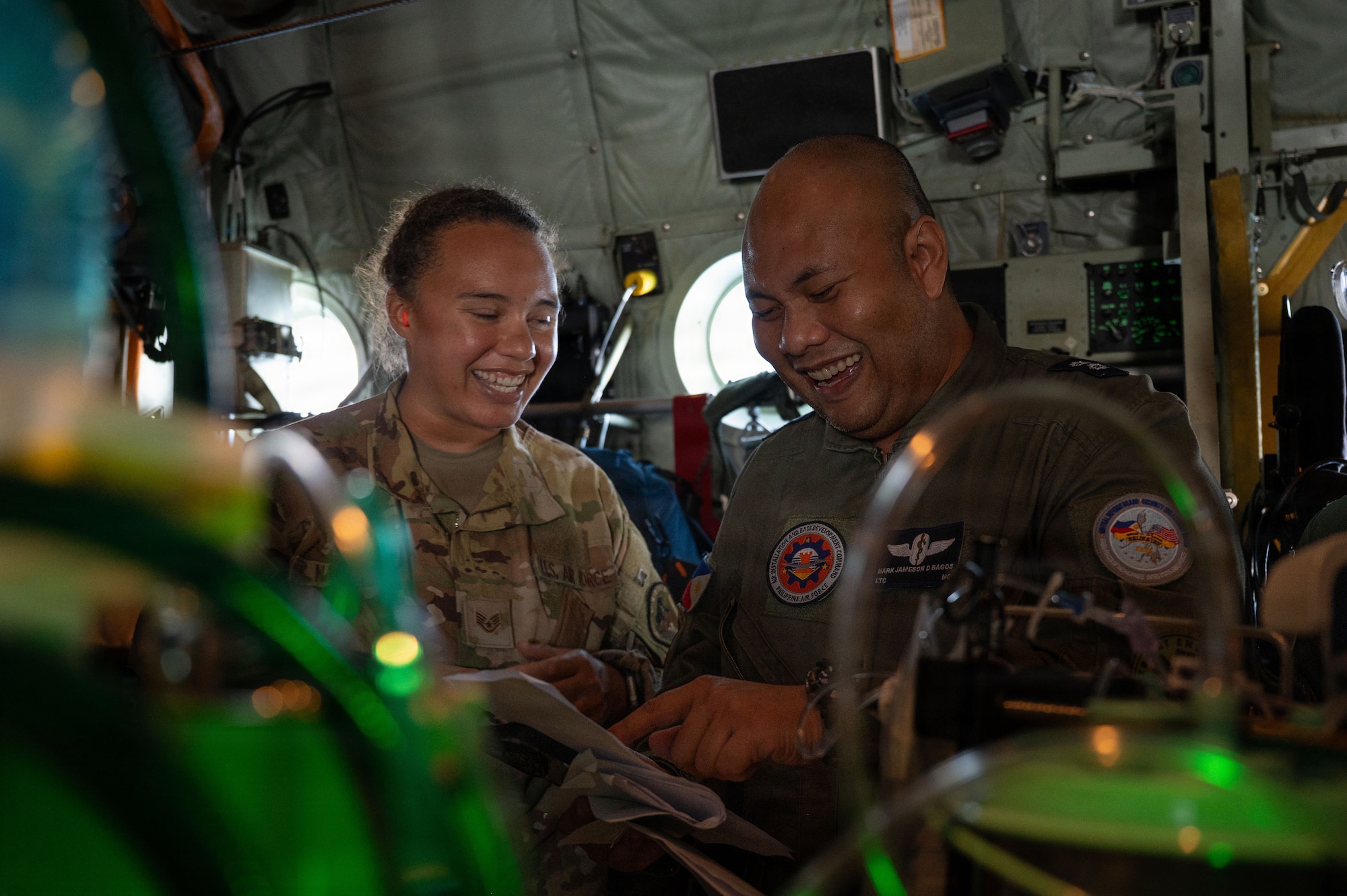 U.S. Air Force Staff Sgt. Sean Napier and Philippine Air Force Lt. Col. Mark Jameson Bagos laugh together while reviewing documents inside a military aircraft.
