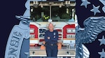 Man in blue pants and shirt, mustache, eye glasses and bald head smiles and poses in front of fire truck with arms crossed.