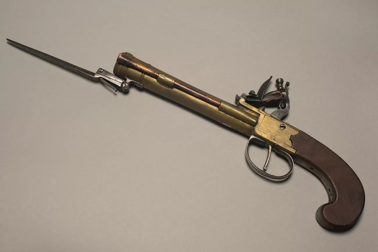 A wood and brass pistol with a small bayonet is on display.
