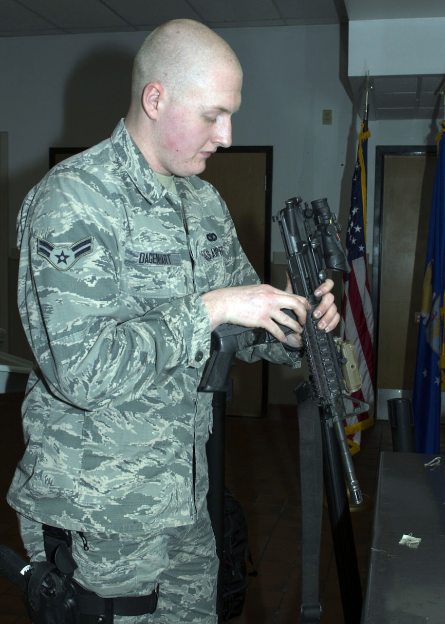 A man wearing a camouflage uniform inspects a weapon in an armory.