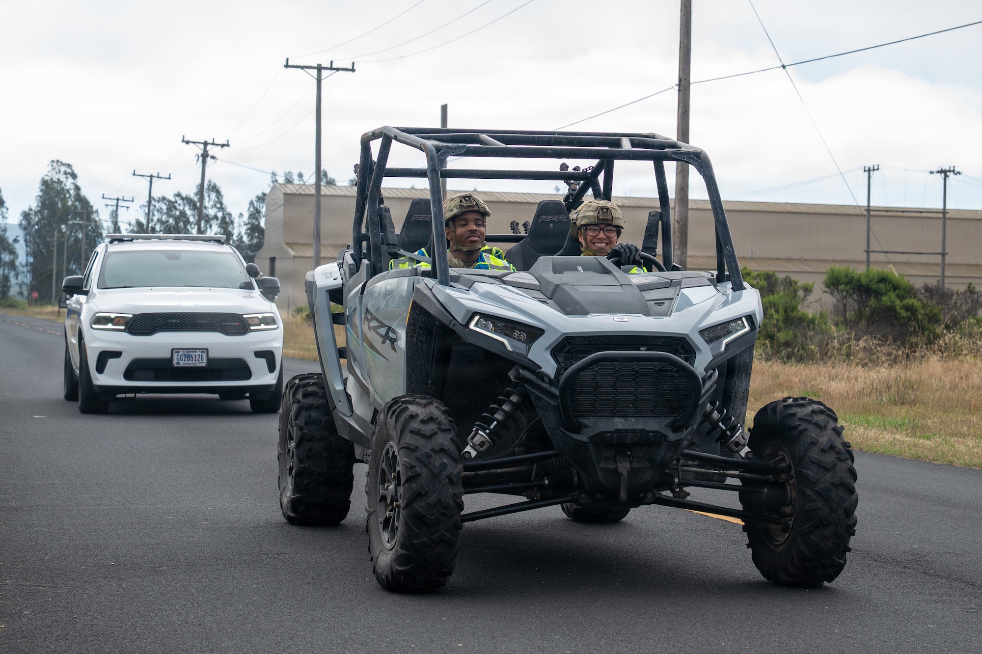 Two servicemembers ride in a razor in front of a police vehicle driving close behind.