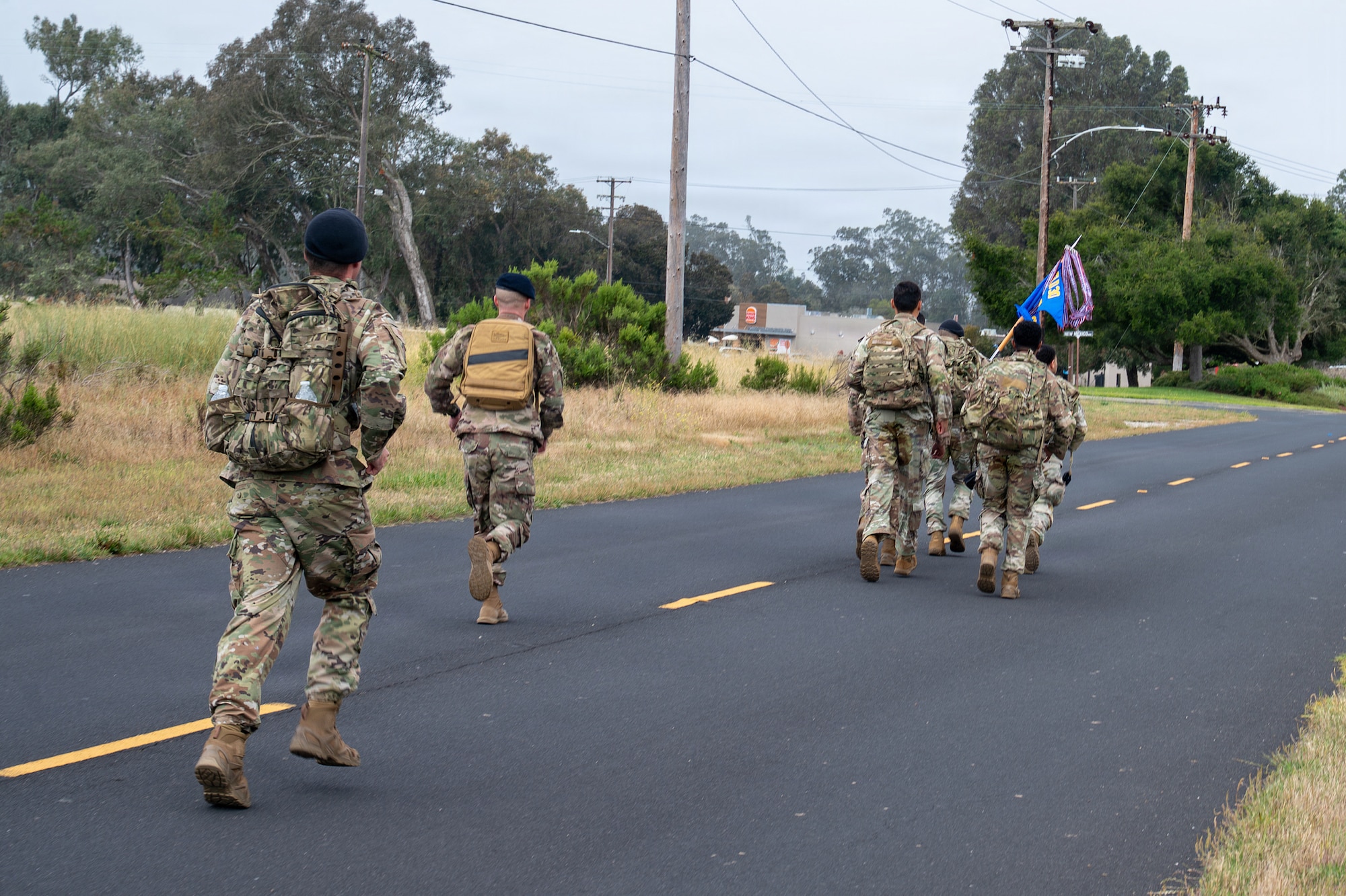 People lightly jog on a road outside, one individual is holding a guide on flag.