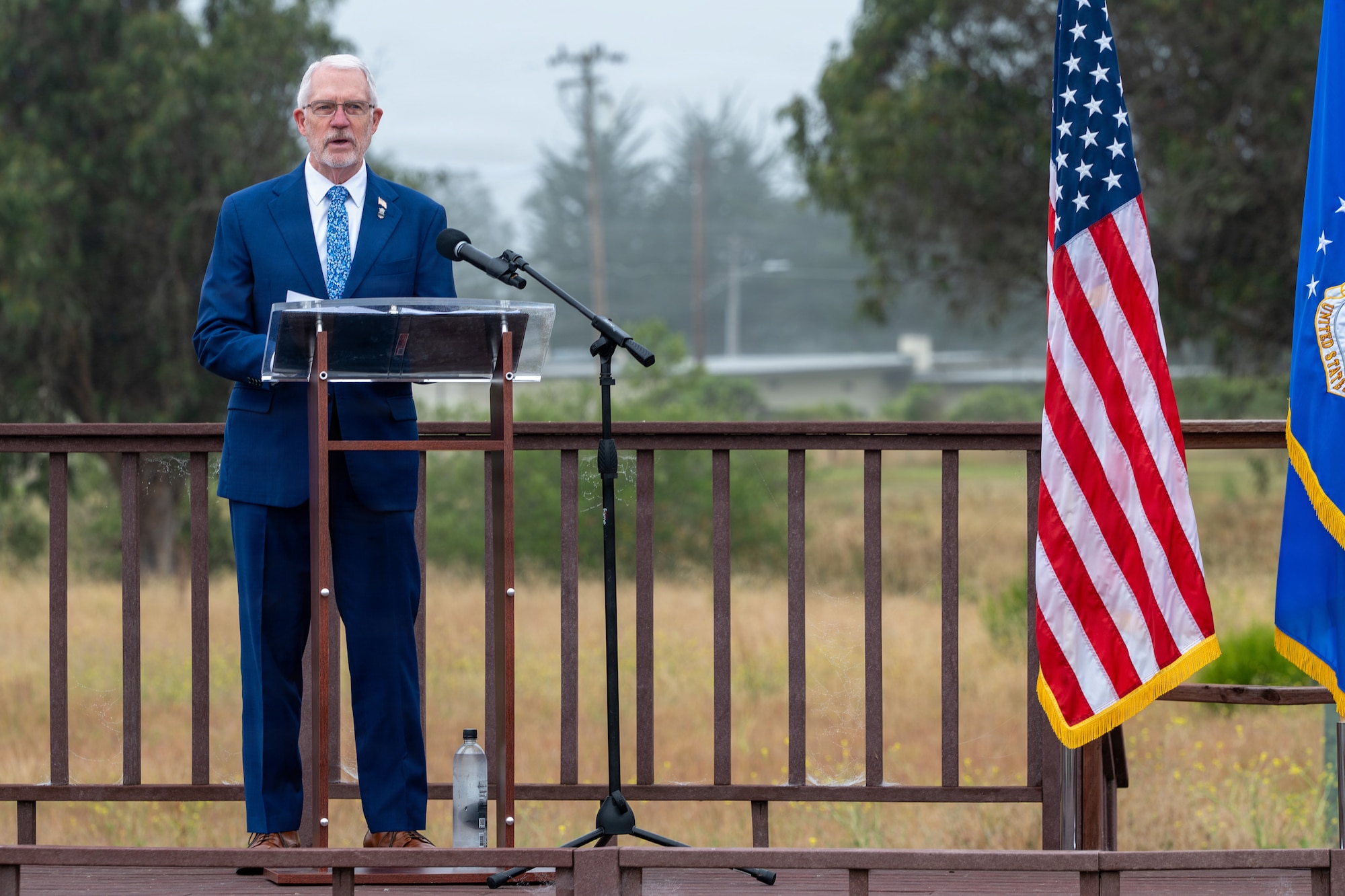 Retired U.S. Air Force Col. John W. Probst, Air Force Security Forces Association executive director, stands and speaks behind a podium on a stage outside.