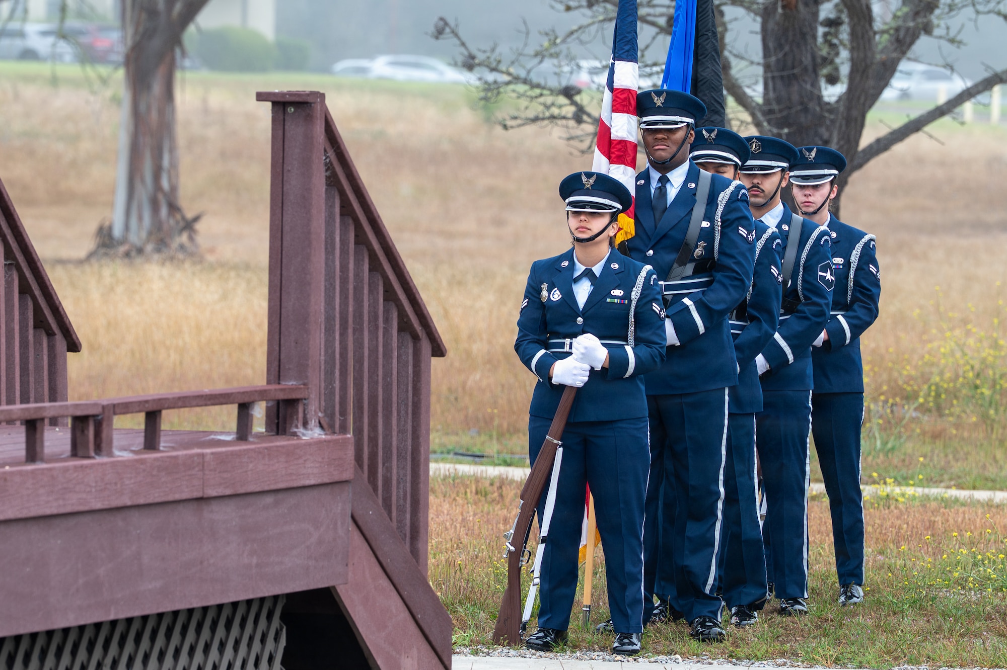Honor Guard members line up behind each other next to a stage outside.