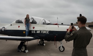 An instructor pilot assigned to the 47th Flying Training Wing takes a photo of a military spouse standing atop the wing of a T-6 Texan II during Military Spouse Appreciation Day at Laughlin Air Force Base, Texas, May 8, 2026. Military spouses and families were able to take photos next to a T-6 and T-38 Talon during the event. (U.S. Air Force photo by Airman 1st Class Darryl Keith)