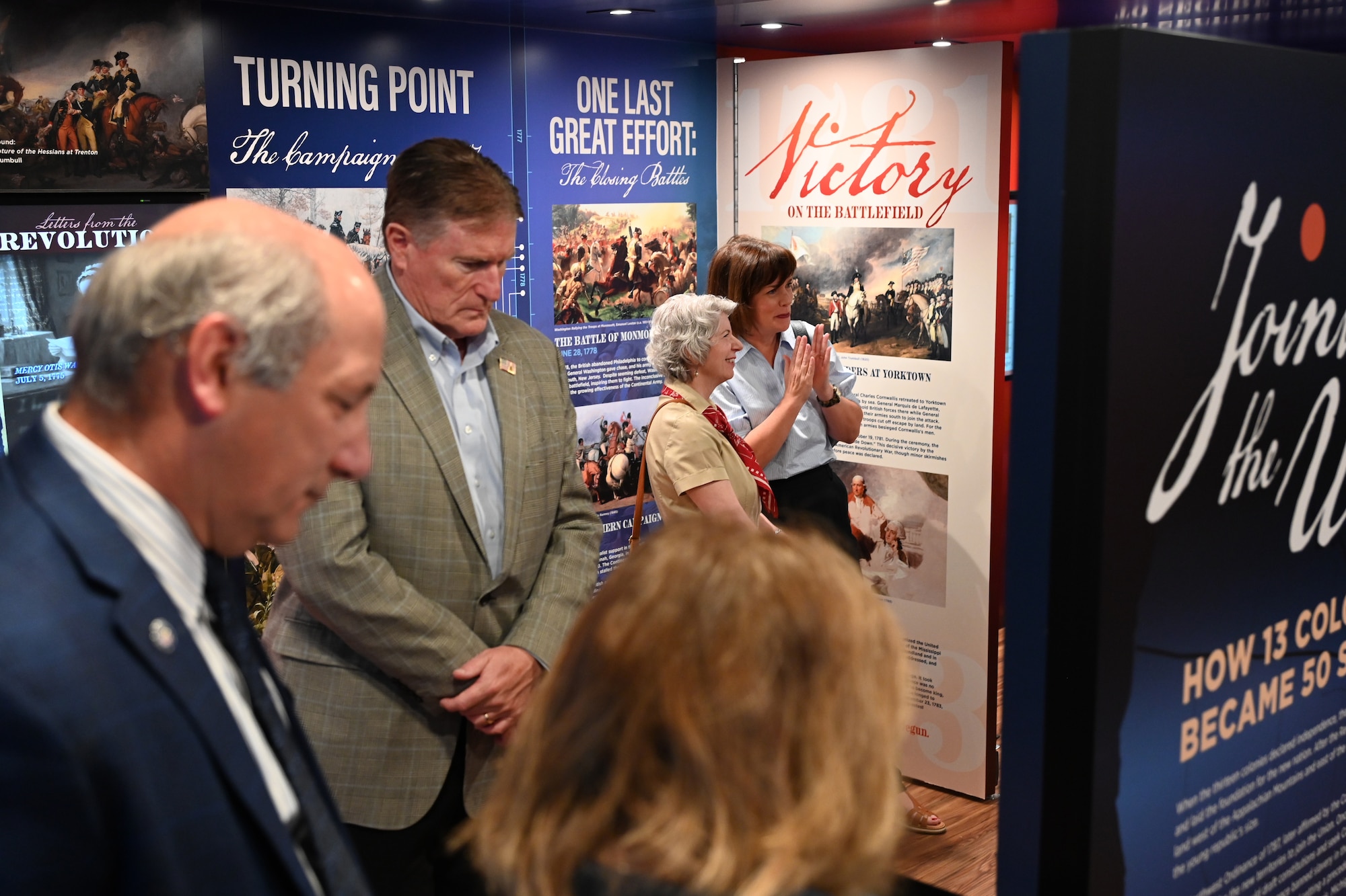 A group of people walk through the interior of the Freedom 250 Mobile Museum, viewing historical displays and informational panels.