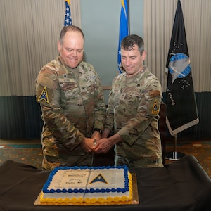 Two people stand near each other holding a cutting utensil and cut the cake together.