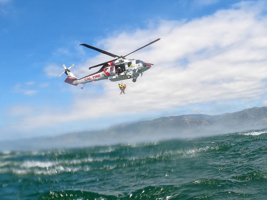 A helicopter over water hoisting people up