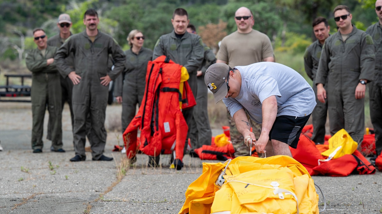 A man demonstrates how to open a raft to a group of people.