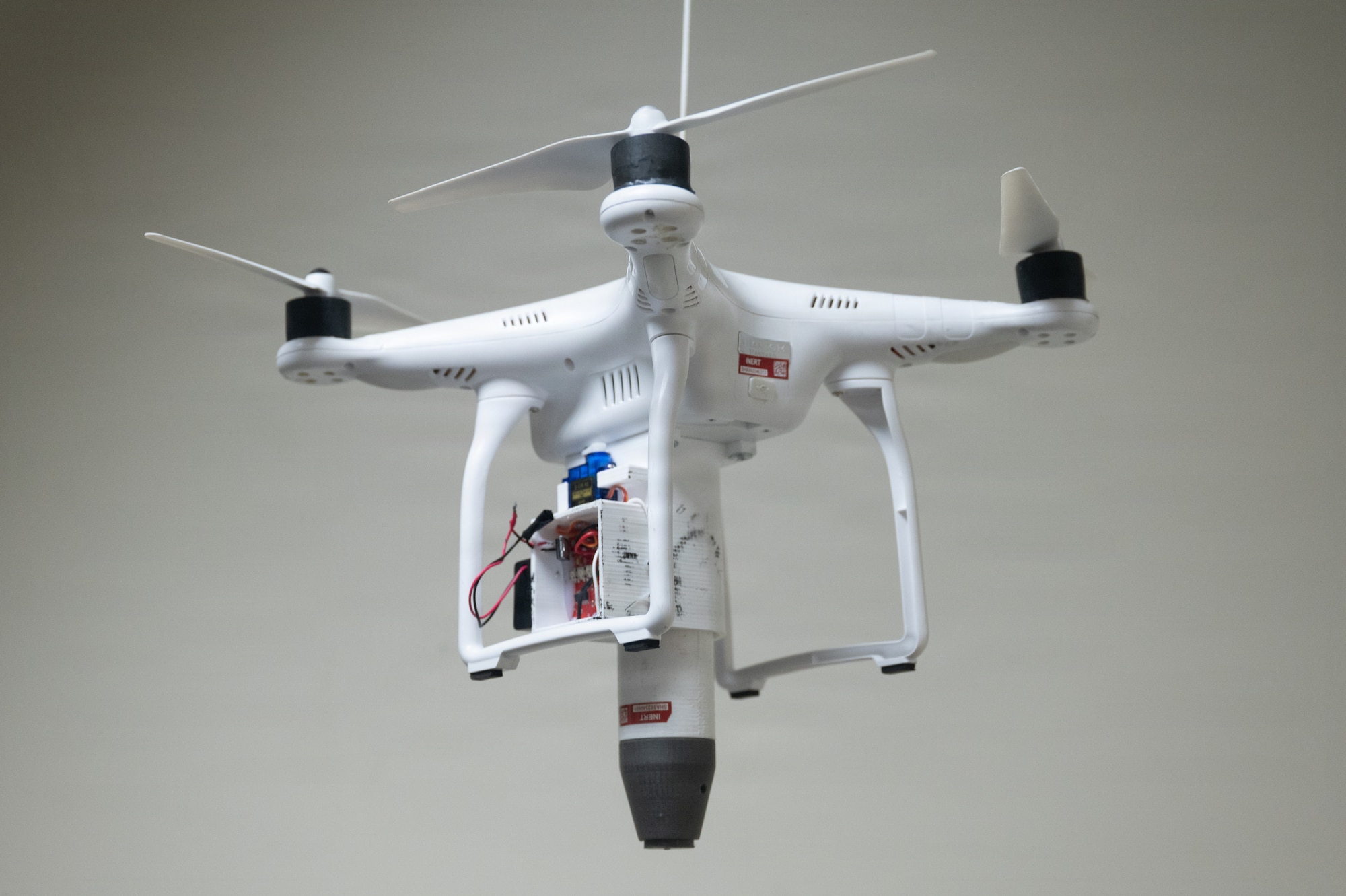 A quadcopter drone equiped with a payload carrier is suspended from the ceiling in a classroom at Joint Base Elmendorf-Richardson, Alaska, Jan. 28, 2026. Even small drone models can carry payloads up to two pounds, including potentially explosive materials. U.S. Air Force photo by Airman 1st Class Theodore Gowdy)