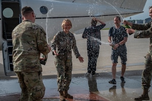 Air Force officers spray champagne from glass bottles at female Lt Gen general in front of white airplane.