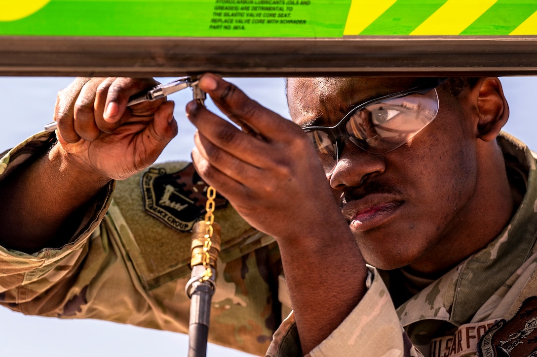 A close-up of an airman using a tool attached to a black hose on an aircraft's boom during the day.