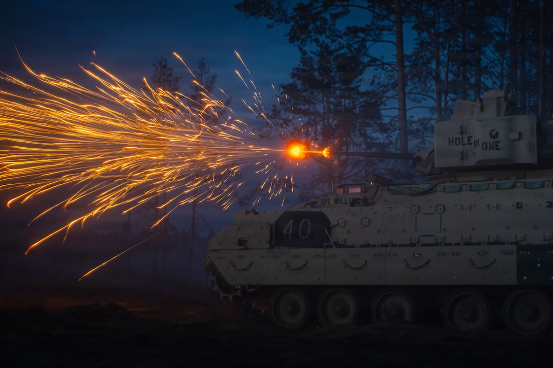 A military fighting vehicle fires into a dark sky, creating dozens of golden streaks.