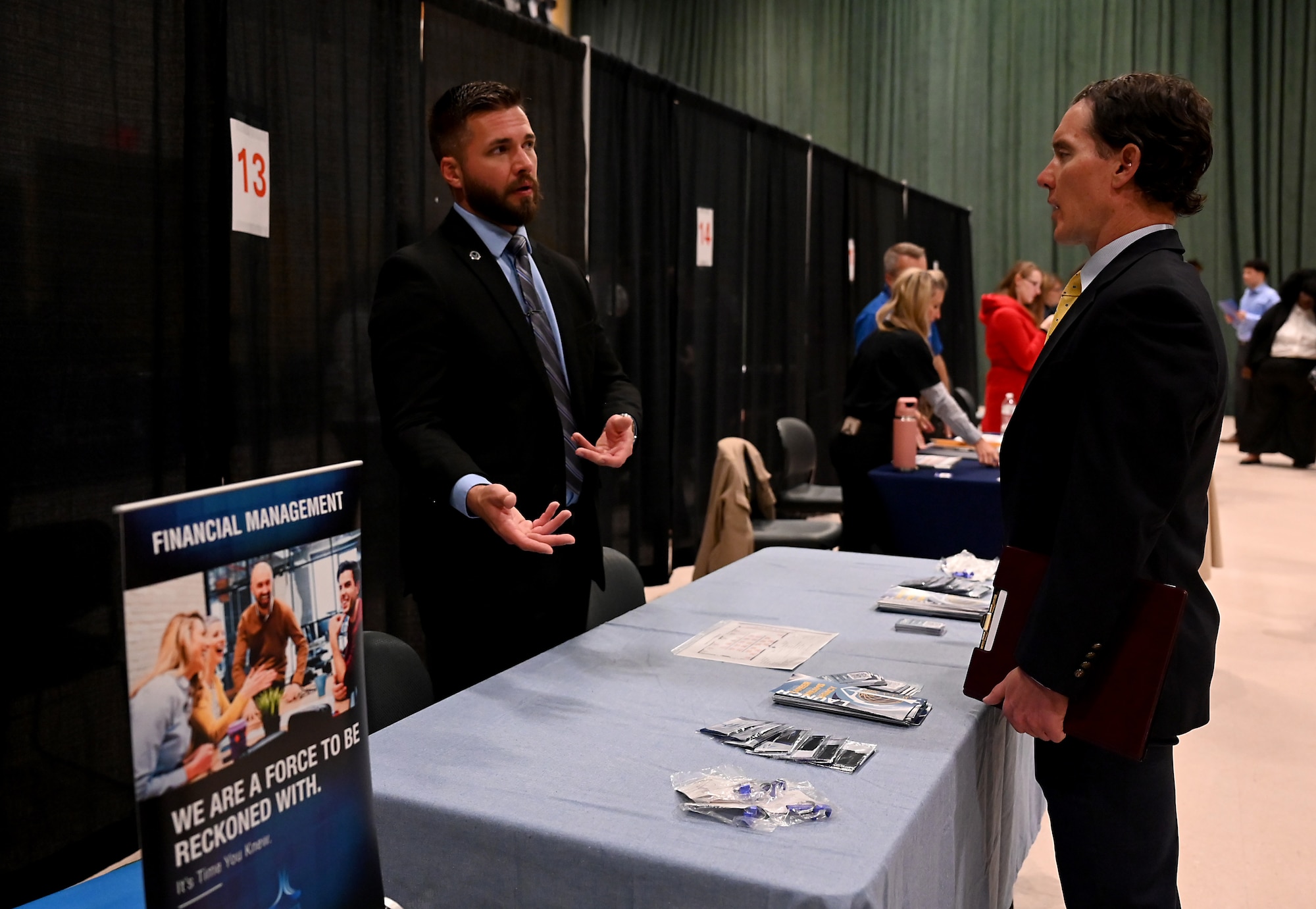 A man in a suit uses his hands to describe something with AFLCMC financial management to another man in a suit.