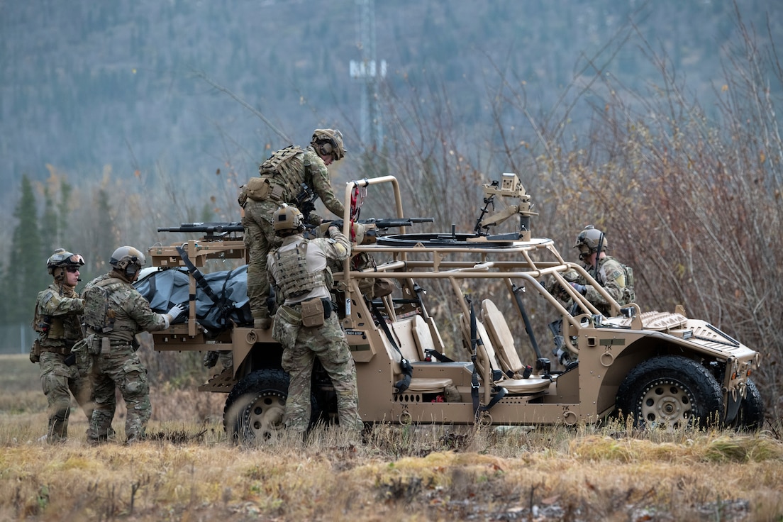 Four men wearing combat fatigues loading a stretcher onto a military ATV.