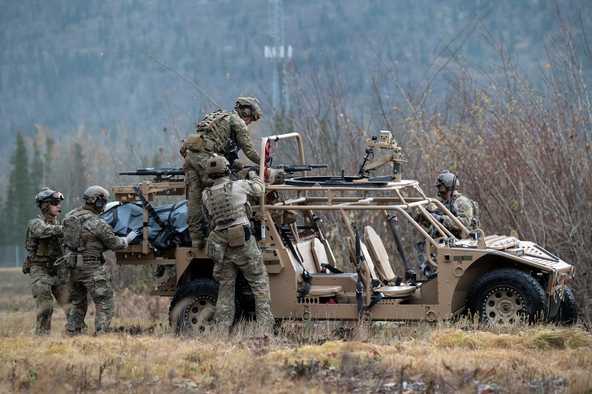 Four men wearing combat fatigues loading a stretcher onto a military ATV.