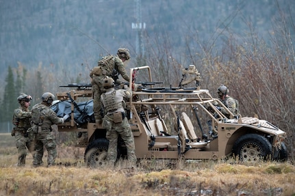 Four men wearing combat fatigues loading a stretcher onto a military ATV.