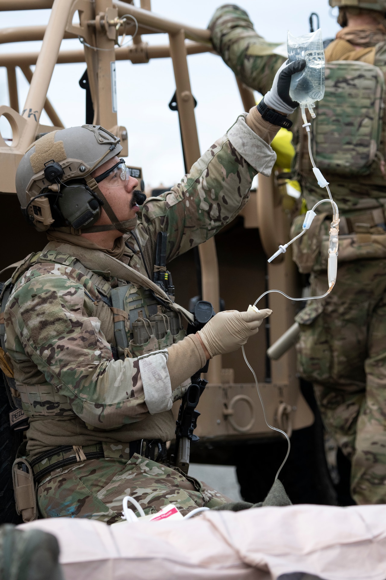 A man wearing camouflage fatigues holding up an IV bottle.