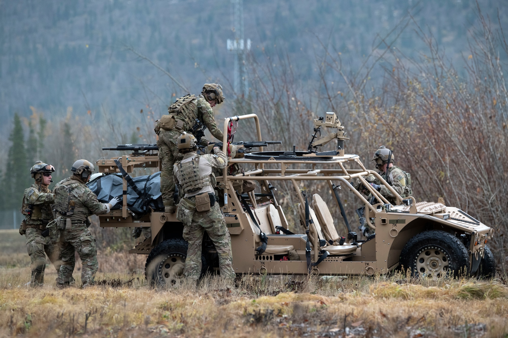 Four men wearing combat fatigues loading a stretcher onto a military ATV.