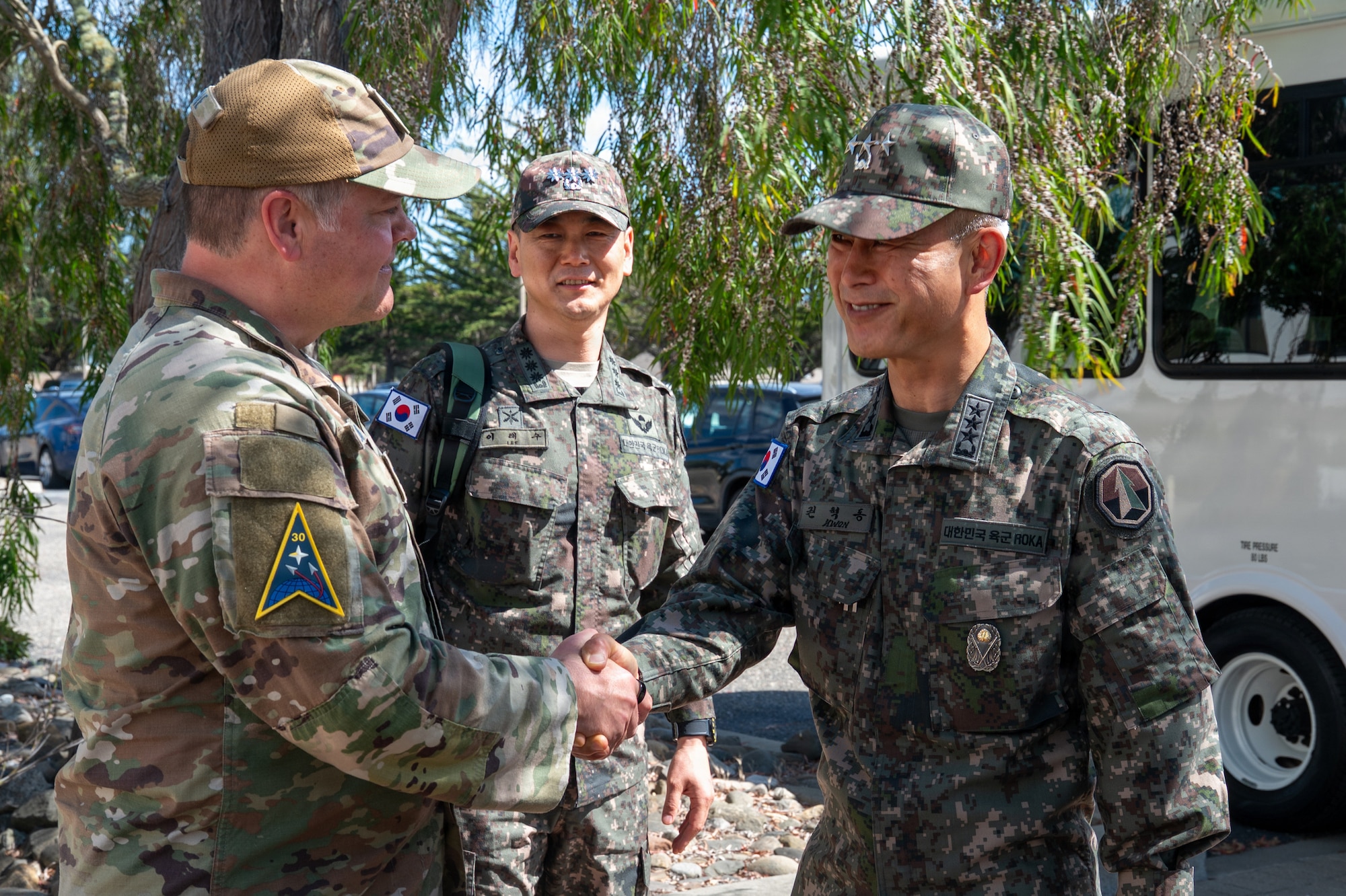 Two people shake hands while another person acknowledges in the backgroud.