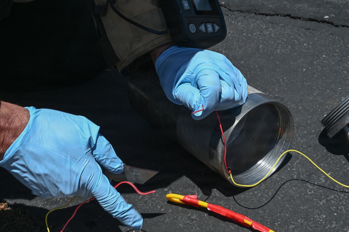 U.S. Air Force Tech. Sgt. Bruce Noble, 355th Civil Engineer Squadron explosive ordnance disposal team leader, cuts the wire to separate initiators from simulated bulk explosives during exercise Mosaic Lightning 26-2 at Davis-Monthan Air Force Base, Arizona, May 8, 2026. The initiators were placed in a metal canister designed to withstand the detonation of a bomb. (U.S. Air Force photo by Staff Sgt. Kahdija Slaughter)