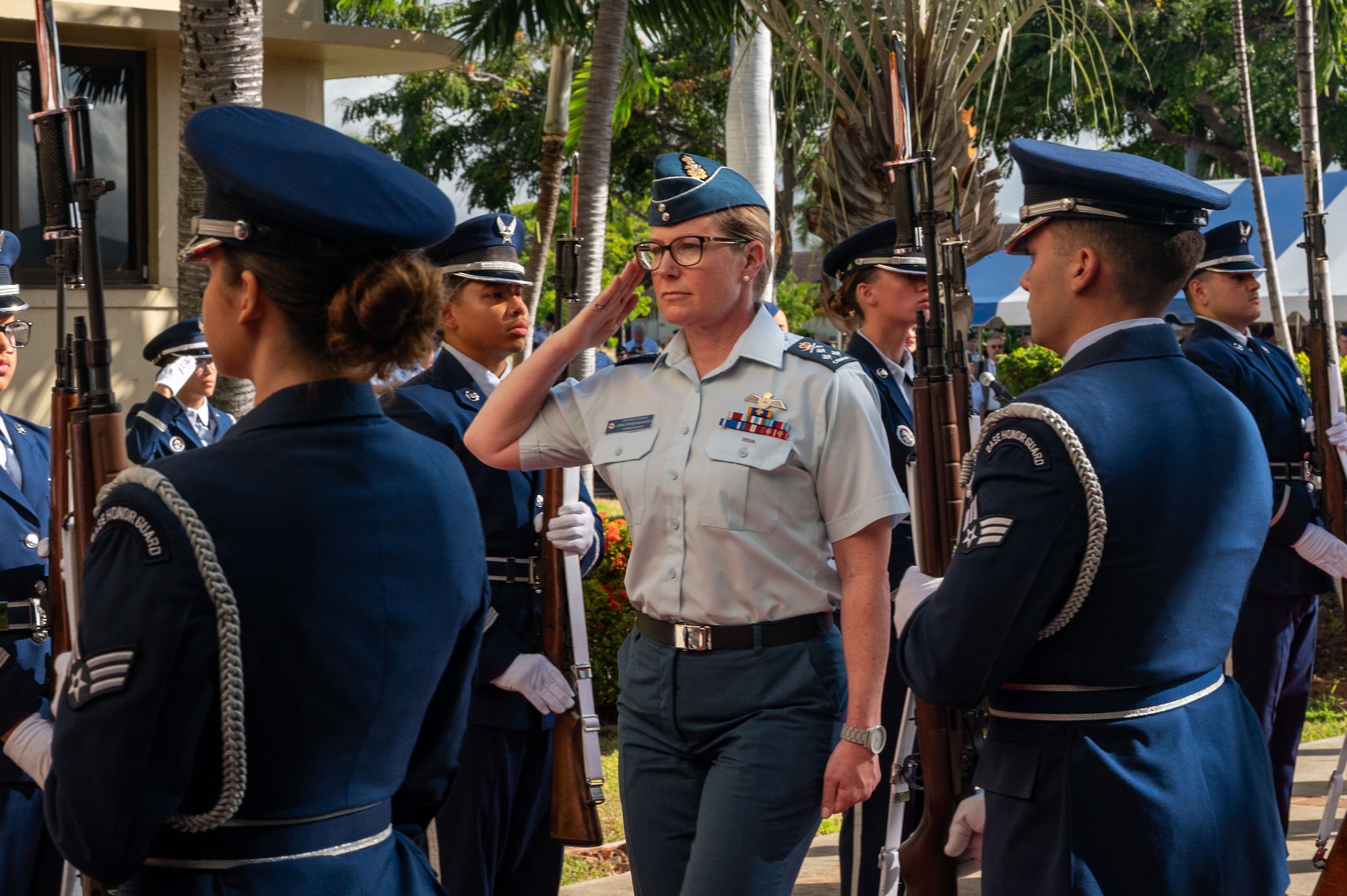 Royal Canadian Air Force Lt. Gen. Jamie Speiser-Blanchet, in uniform, renders a salute while walking through an honor cordon formed by U.S. Airmen in dress uniforms. The ceremony takes place outdoors, with palm trees visible in the background.