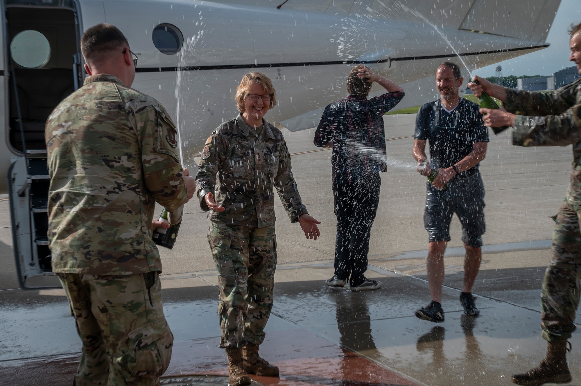 Air Force officers spray champagne from glass bottles at female Lt Gen general in front of white airplane.