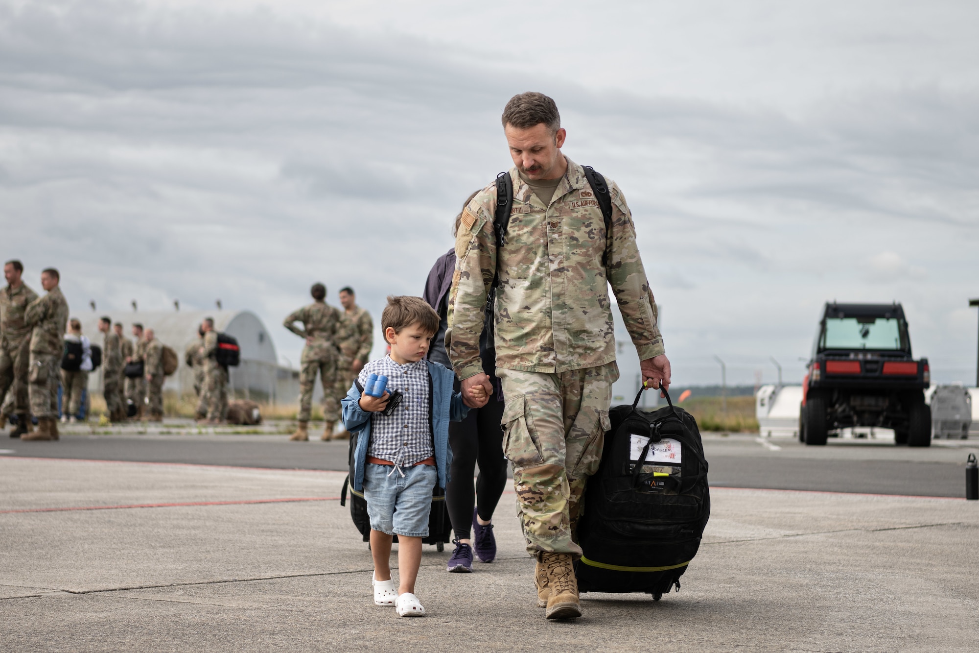 A father walks with his young son and a suitcase.