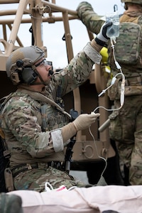 An Alaska Air National Guardsman assigned to the 212th Rescue Squadron, 176th Wing, prepares an intravenous line while responding to a simulated mass-casualty incident during a full mission profile exercise at Joint Base Elmendorf-Richardson, Alaska, Oct. 13, 2021.