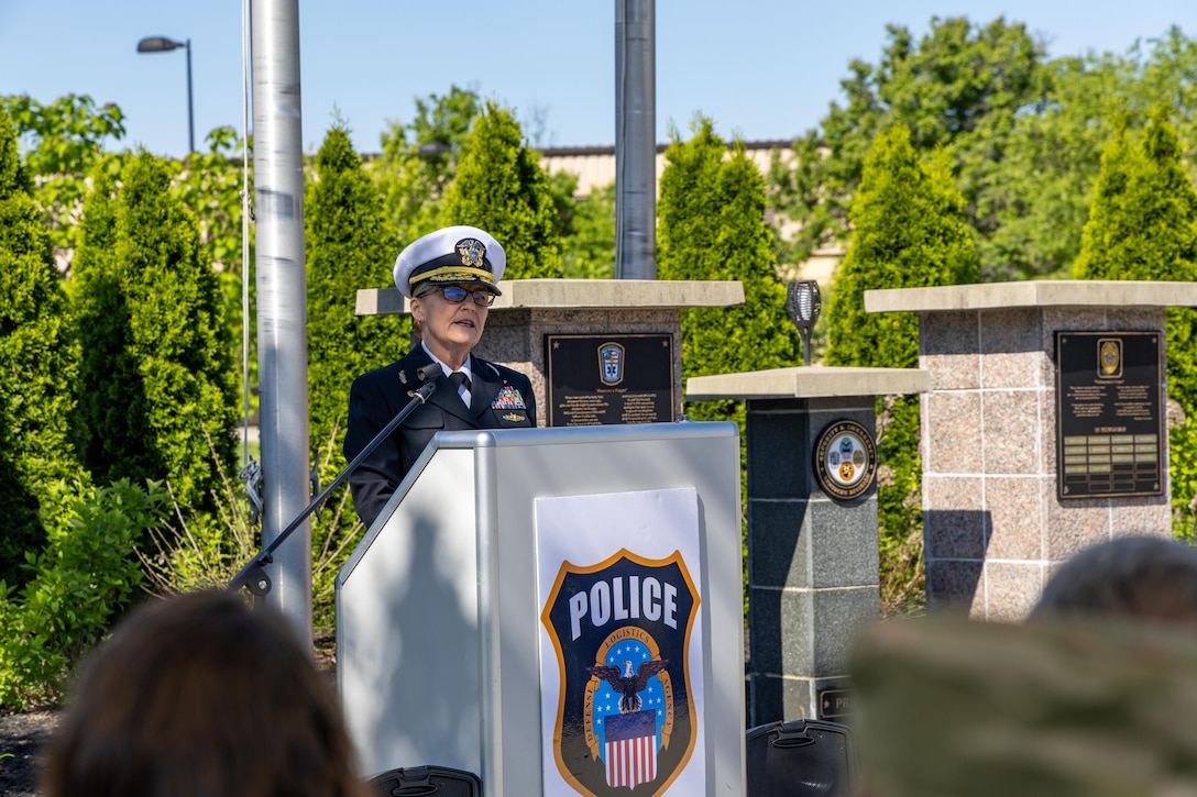 Woman in Navy uniform, white hat stands behind podium with Police badge on it.