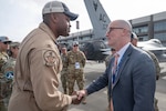 A uniformed service member shakes hands with a person in business attire while standing on a tarmac during daylight.