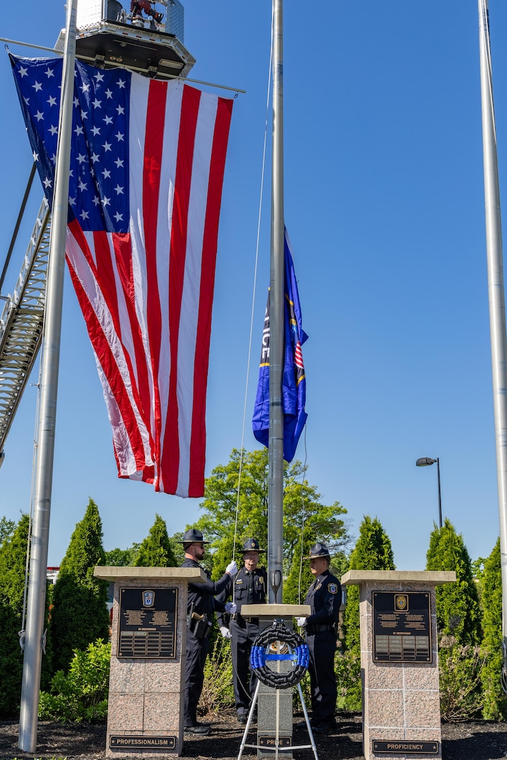 Three police officers raising flag with large American flag hanging from fire ladder behind.
