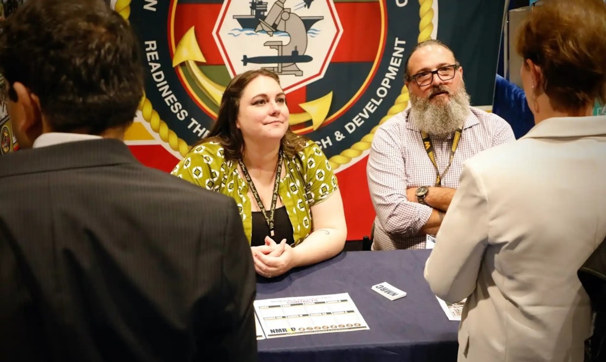 KISSIMMEE, Fla. (Aug. 4, 2025) Emily Swedlund, with Naval Submarine Medical Research Laboratory (NSMRL), and Tommy Lamkin, with Naval Medical Research Command (NMRC), speak with attendees at the Navy Medicine Research and Development (NMR&D) exhibit booth at the 2025 Military Health System Research Symposium (MHSRS).