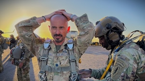 A U.S. Soldier assists a U.S. Guardian in donning his parachute before an airborne operation.