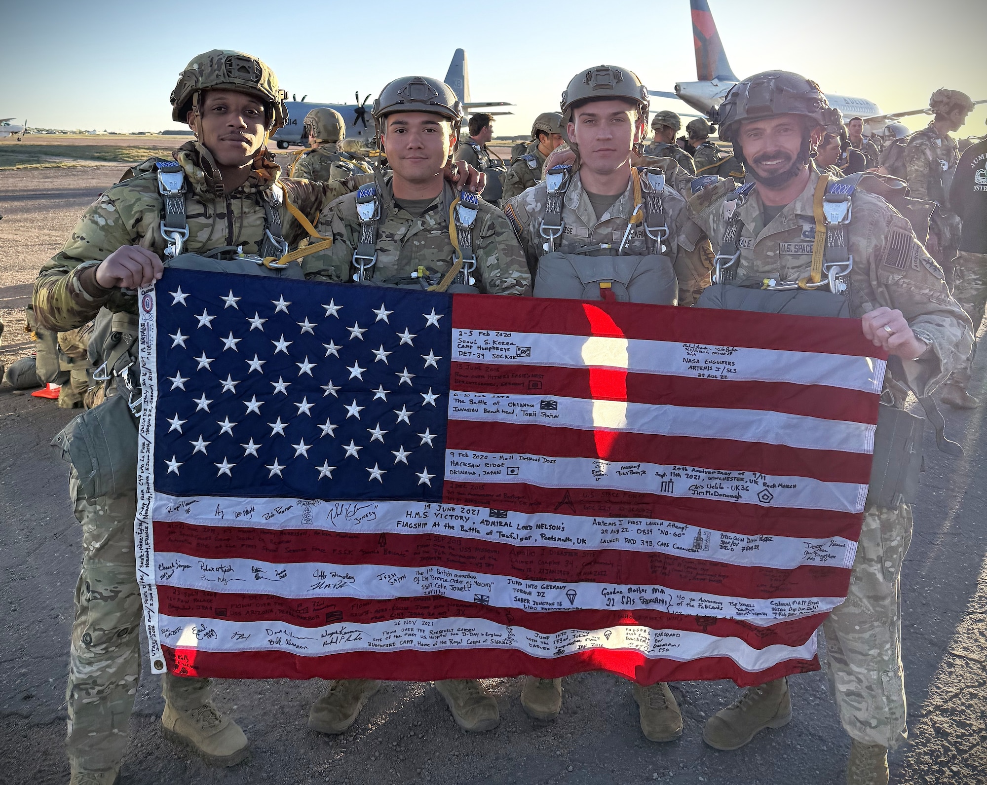 Four U.S. Service members in uniform pose for a photo while holding an American flag